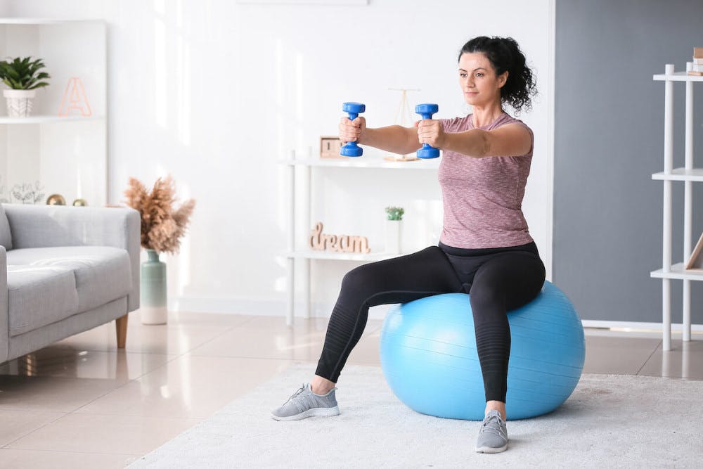 woman-exercising-using-a-pilates-ball-and-dumbells